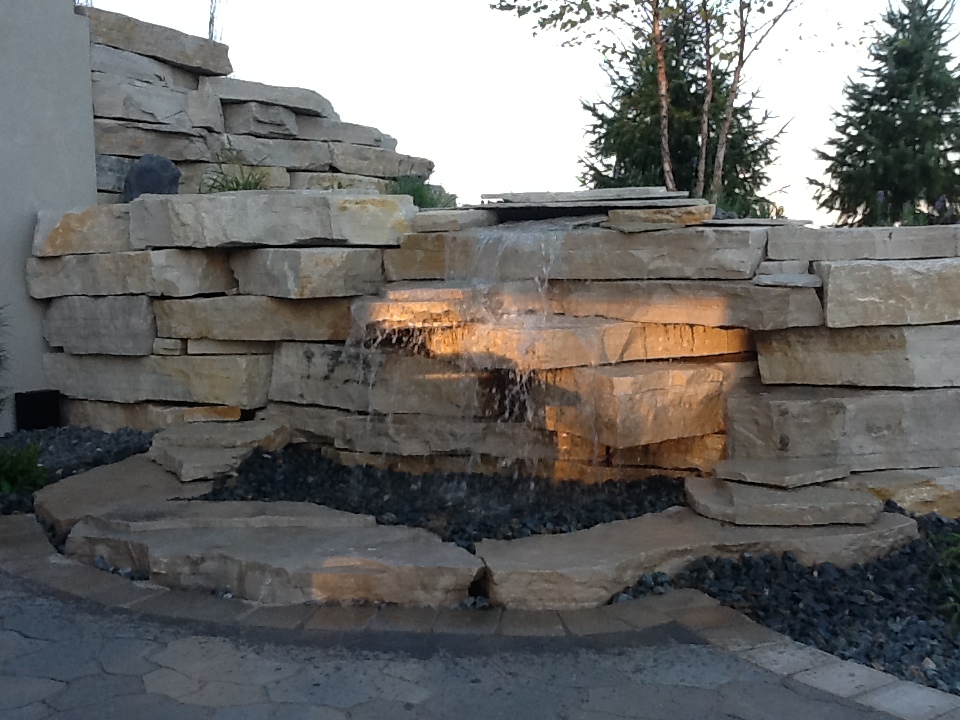 cascade water feature along stone retaining wall with outdoor lighting