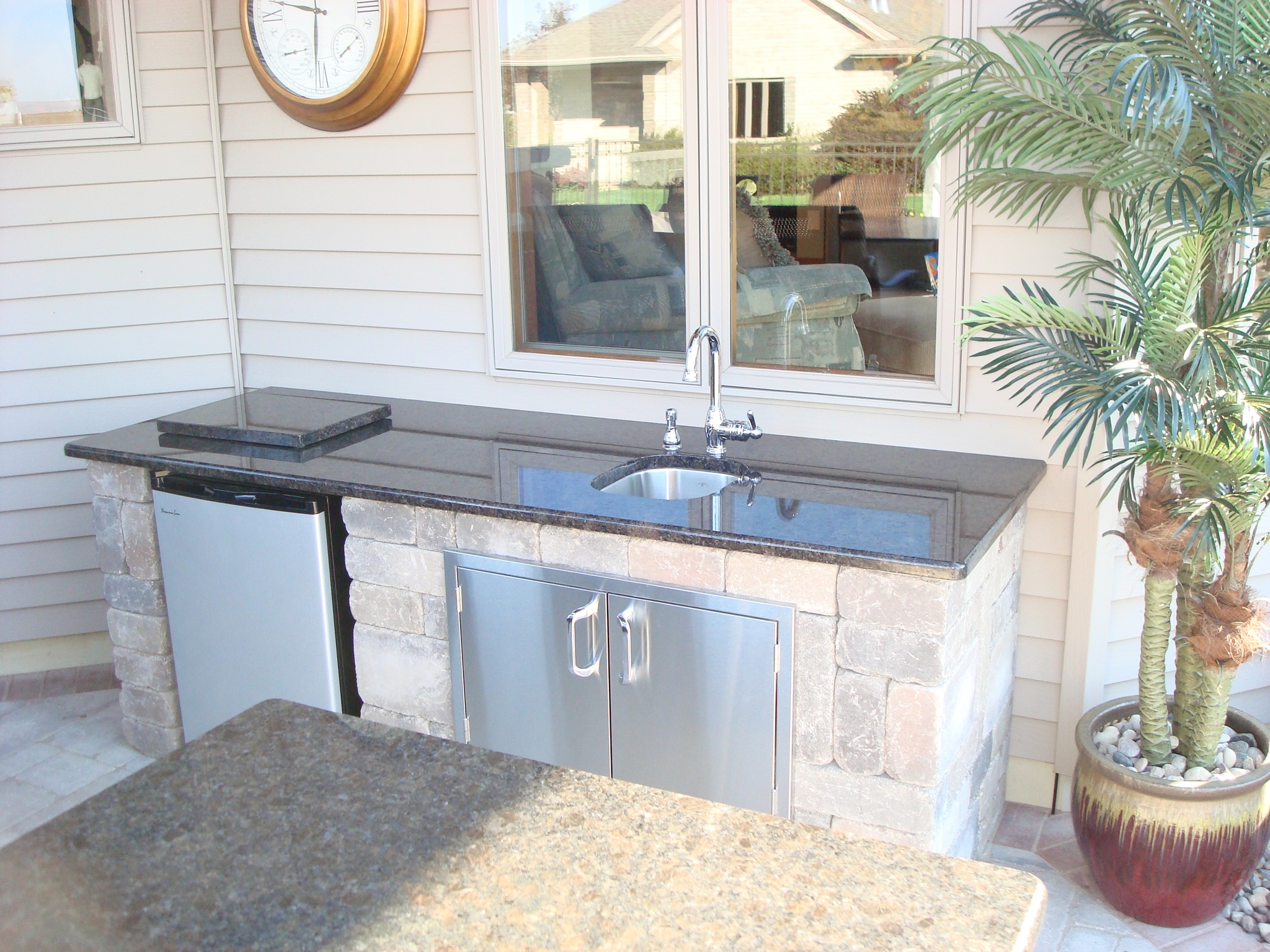Outside kitchen with sink and small refrigerator across from outdoor bar area 