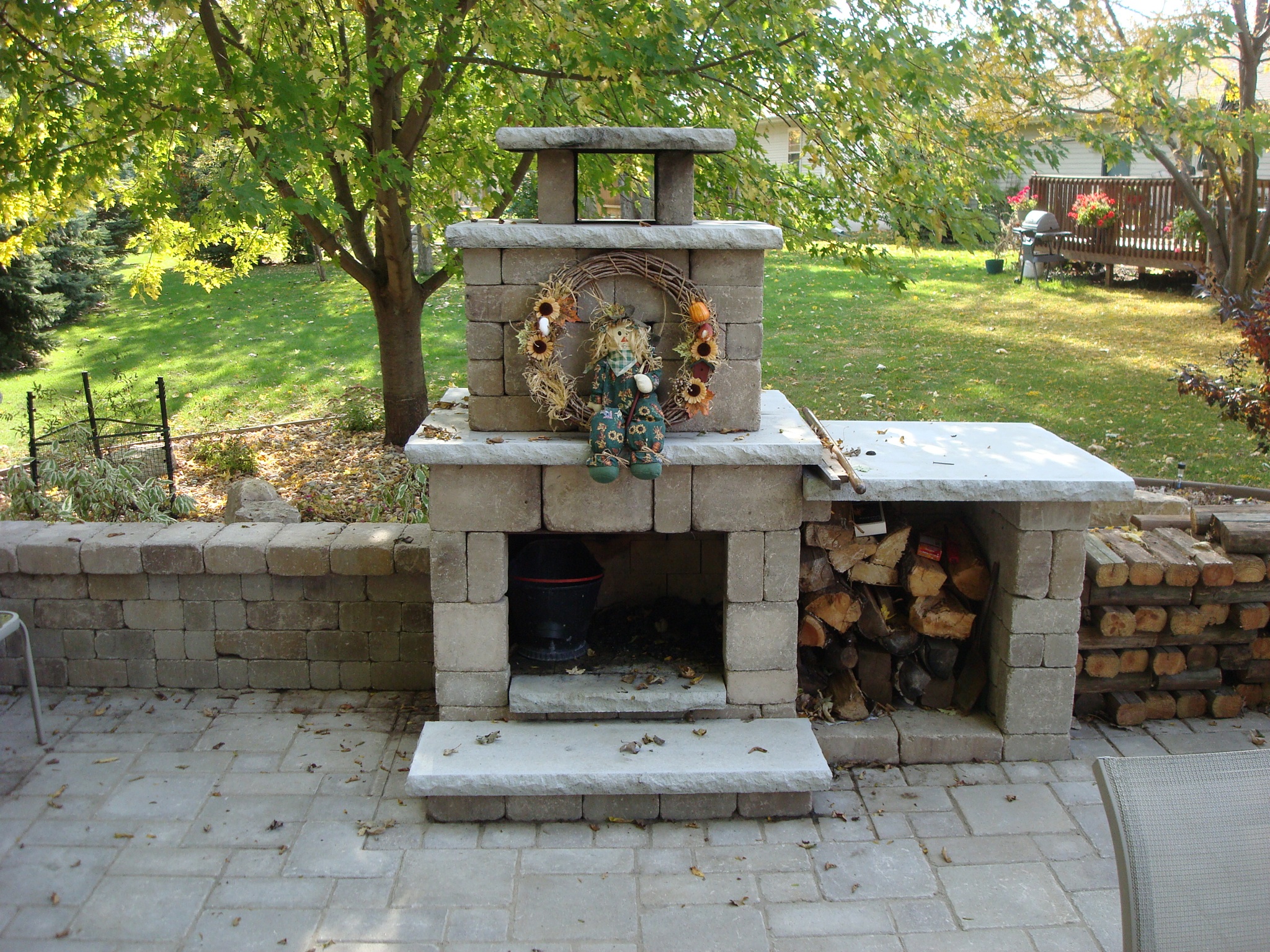 outdoor brick fireplace with two above shelf levels next to wood pile along sit wall
