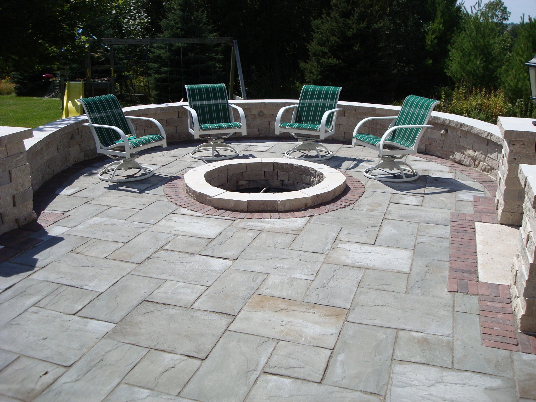 large fire pit in half-circle area of rock tile patio with four green chairs
