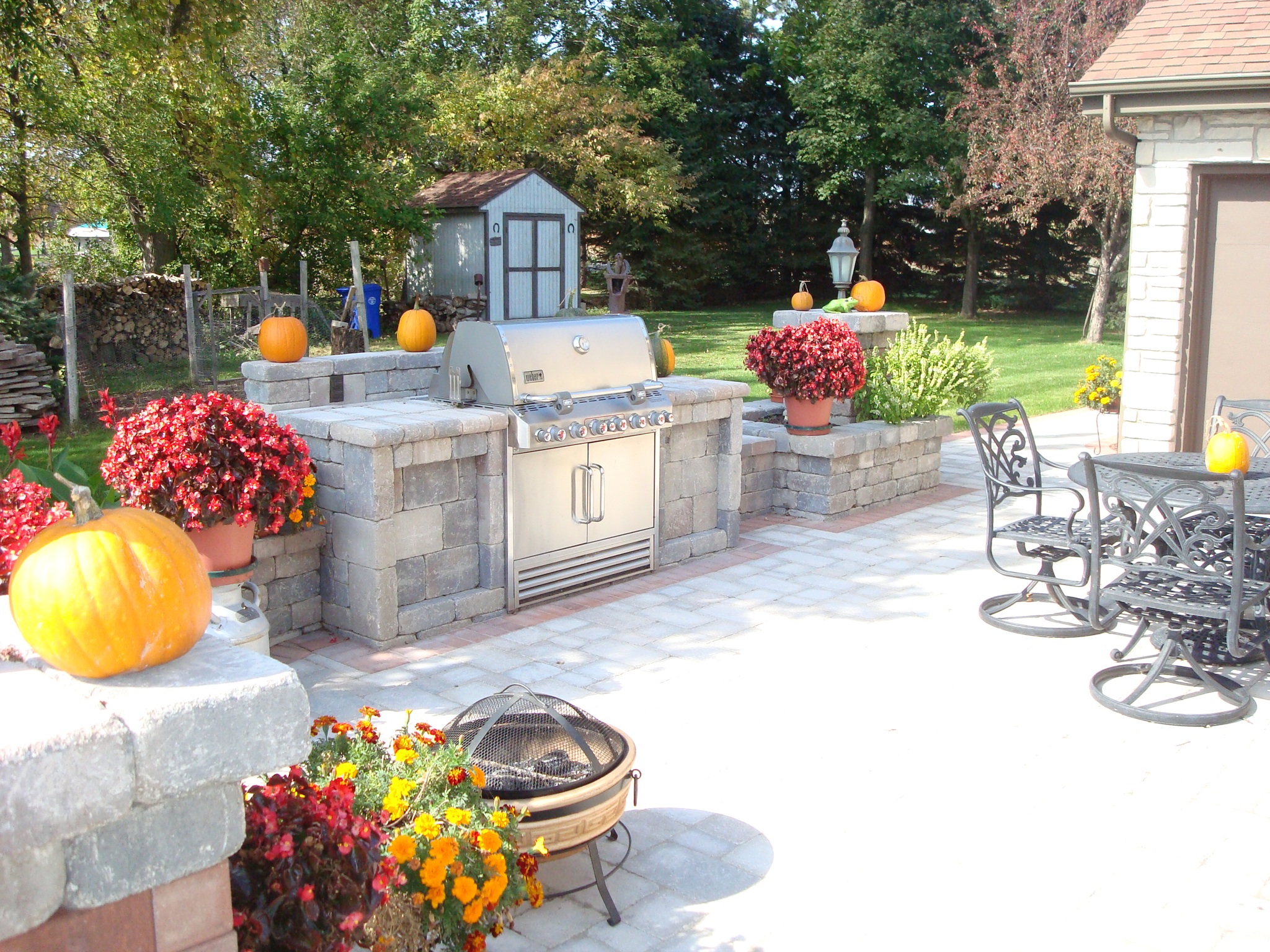 wide-shot of grill and small outdoor kitchen with patio seating area and flower pots